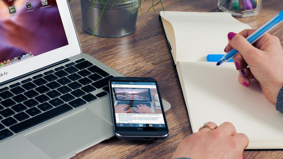 Dizüstü bilgisayar, telefon ve deftere not alan bir el